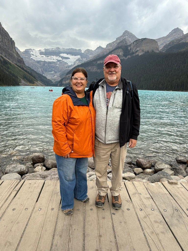 A photo of Natasha and her husband in front of a turquoise colored Lake Louise in Ontario Canada with mountains in the backdrop. Photo permission given to Onward Sister by Natasha Parvey.