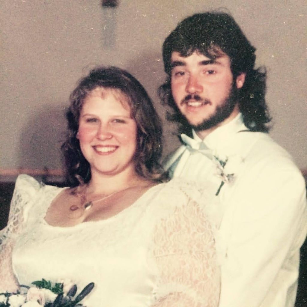 Bryan Mueller in a white tuxedo and Sandi in a white wedding gown with lace sleeves on their wedding day. Photo copyright Sandi Mueller. Permission for use given by Sandi Mueller.