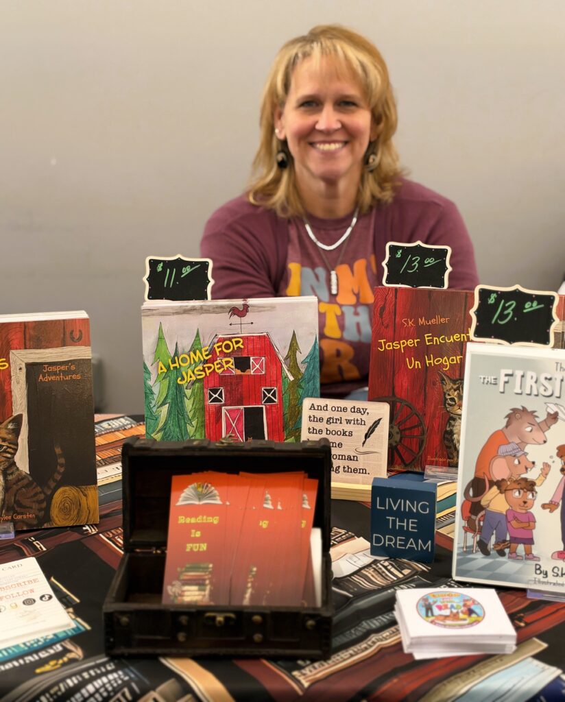 A photo of Sandi sitting behind her priced books at her author's table at the Scappoose Library Author's Festival. Photo taken and copyrighted by Sue Evergreen. Sandi gave Onward Sister permission to use.