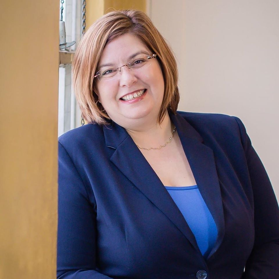 Professional portrait of Natasha Parvey in a classy dark blue blazer over a blue shirt, with gently framed glasses. Image permission was given to Onward Sister by Natasha Parvey.