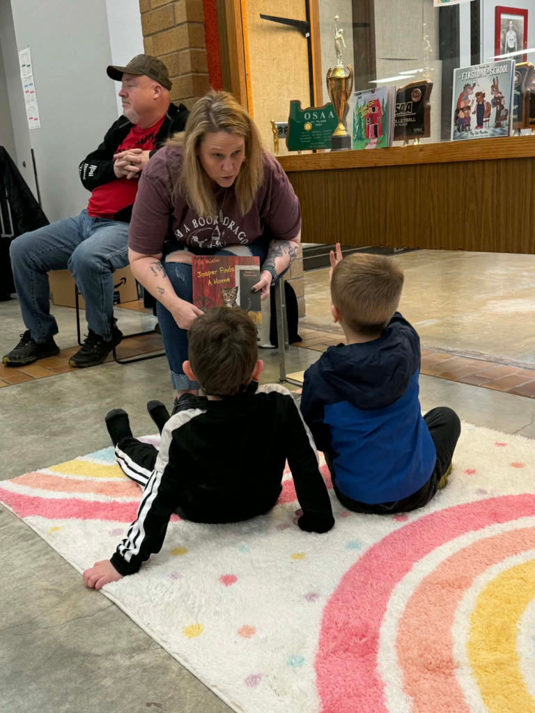 Sandi S.K. Mueller is reading to kids with her husband, Bryan, in the background, listening. Photo copyright: Sandi Mueller. Permission for use given to Onward Sister by Sandi Mueller.